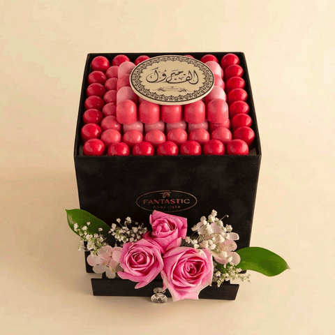 Box of pink and red chocolates with decorative flowers on a beige background